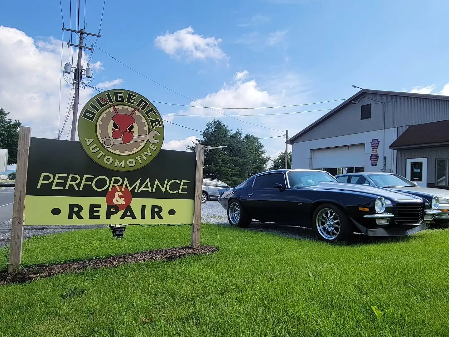 The Diligence Automotive Performance & Repair sign outside the shop, with a classic Camaro parked out front